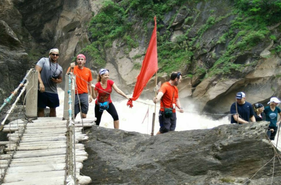 Travelers crossing a mountain footbridge beside a waterfall