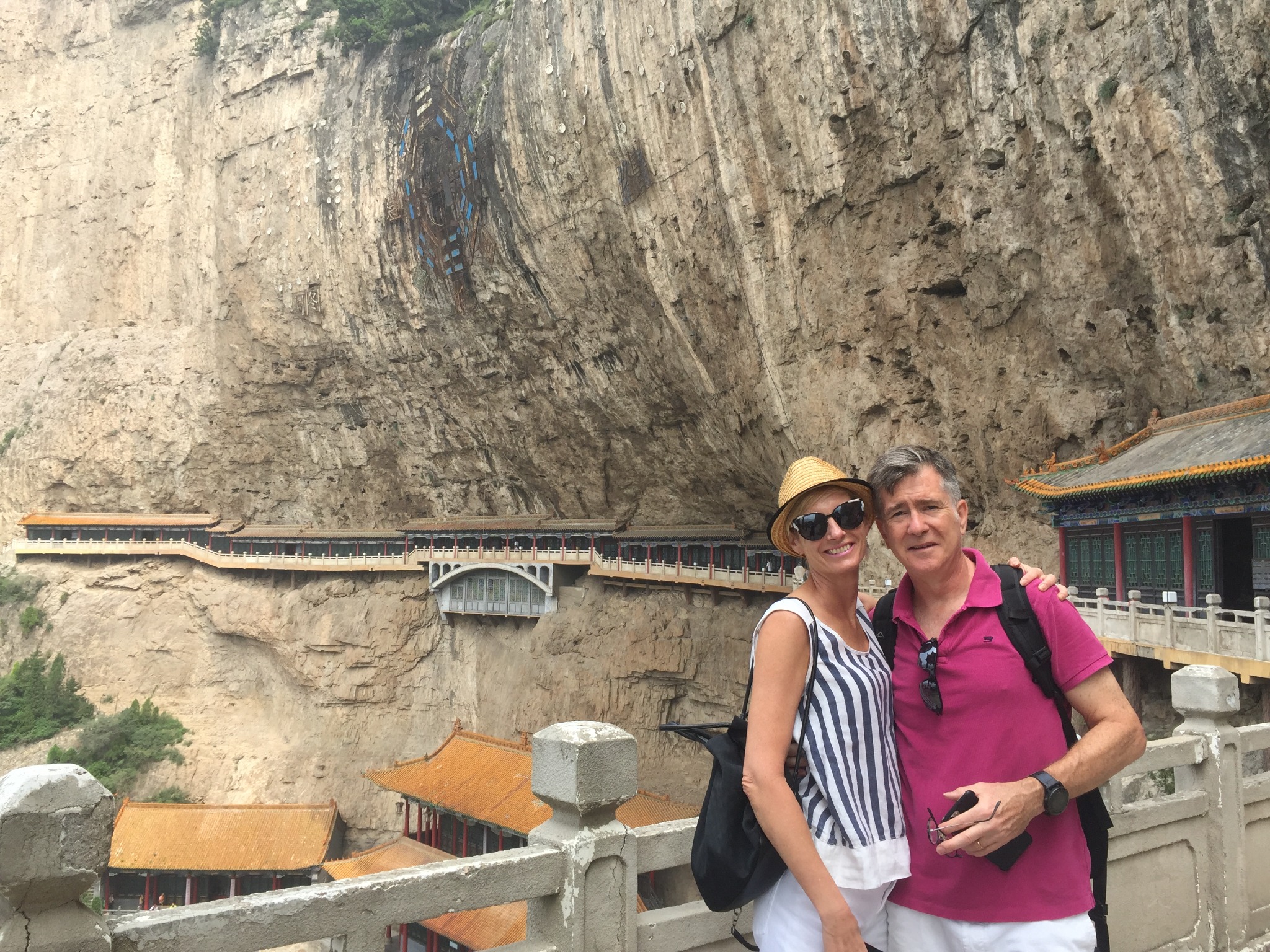 Two travelers beside historic buildings beneath a sheer cliff