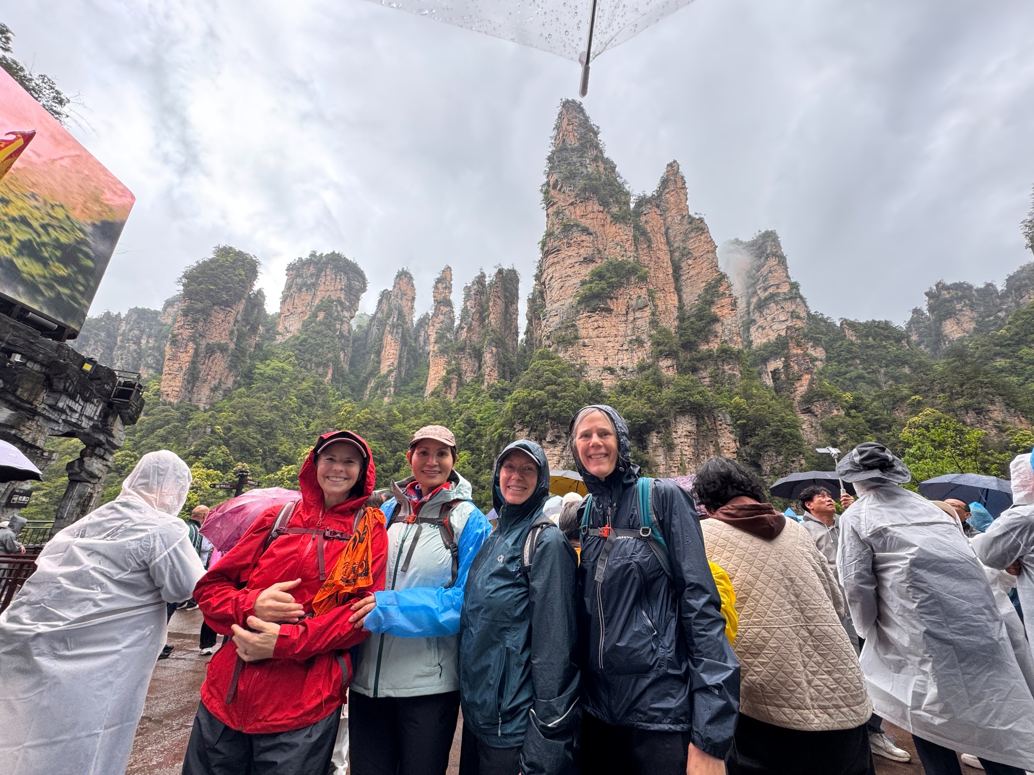Four travelers wearing rain jackets beneath tall sandstone pinnacles