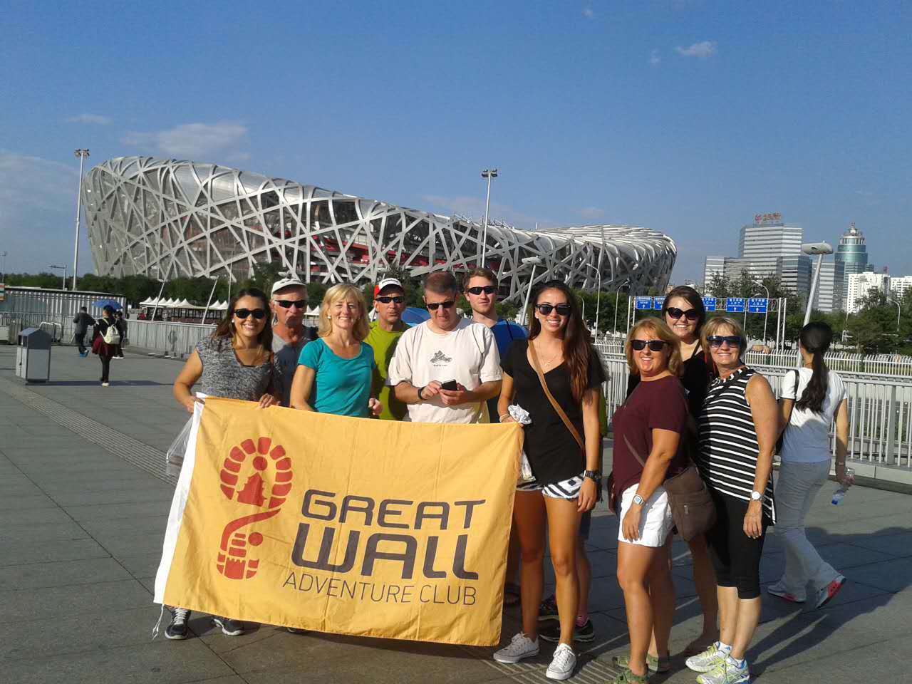 Traveler group holding a Great Wall Adventure Club banner in front of Beijing National Stadium