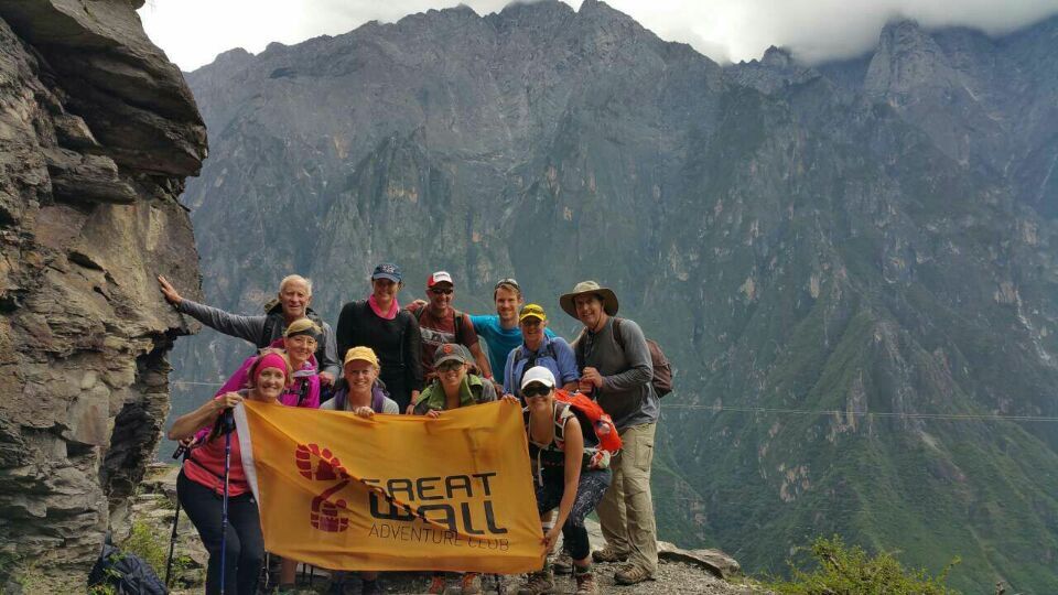 Hiking group holding a Great Wall Adventure Club banner against steep mountain scenery